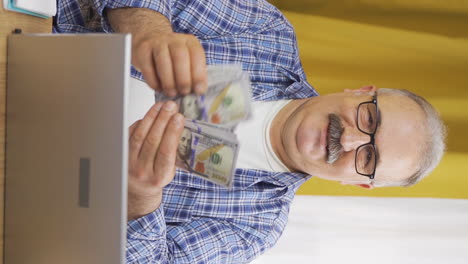 Vertical-video-of-Old-man-looking-at-laptop-counting-money.